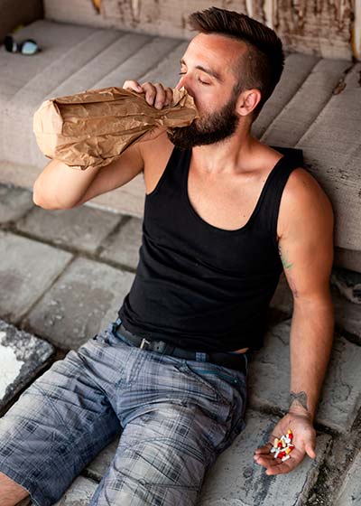 мужчина сидит на земле и пьёт алкоголь из бутылки